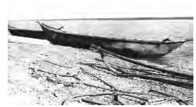 Two moose-skin boats sit on the bank, and the frame of an unfinished boat can be seen in the foreground (1918).