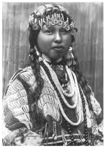 A Wishram bride wears a loop necklace, a dress with six broad rows of lazy-stitch beading on the yoke. She has three strands of white disk shell beads, used as currency, as a necklace. The front of her wedding cap has a row of Chinese coins. 