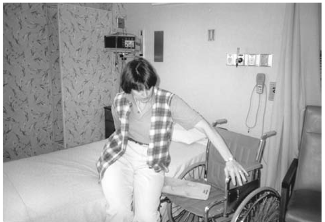 This woman is able to transfer herself independently from bed to chair and back with the use of a transfer board. The right arm rest is removed from the wheel chair, to facilitate transfer.