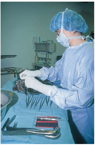 The scrub nurse or technician prepares sterile instruments for the surgeon's use.